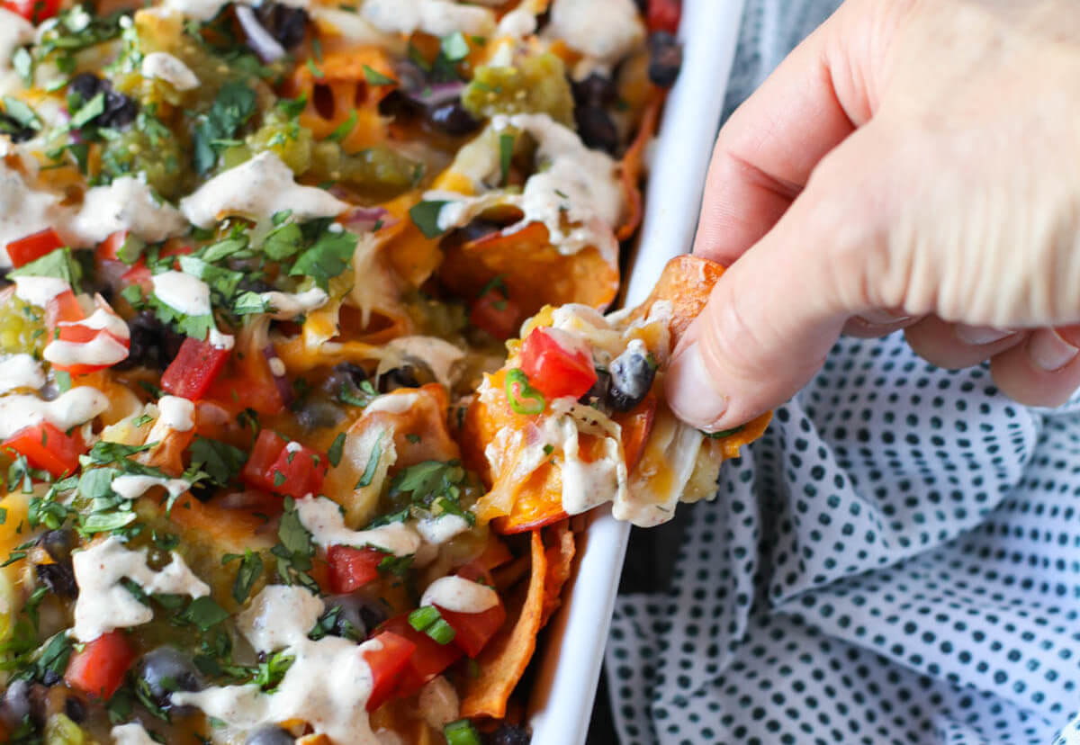 Someone taking a loaded nacho out of the baking dish.